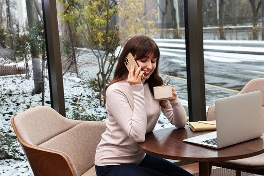 Smiling businesswoman talking by smartphone during coffee break in cafe