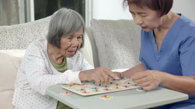 Nurse in nursing home helping elderly woman play number puzzle game. Dementia, Alzheimer's disease.