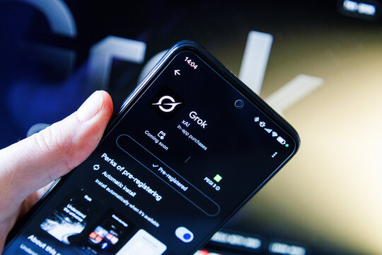 A person holding a smartphone displaying the pre-registration page for the Grok AI app on the Google Play Store
