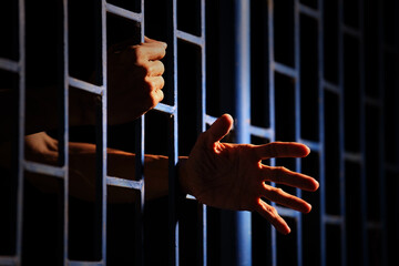 Hands Reaching Through Prison Bars Against Dark Background