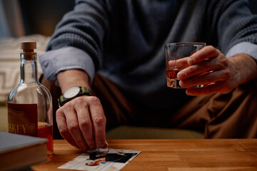 Hand holding whisky glass over photograph on wooden table, bottle of whisky nearby. Arm wearing wristwatch and casually dressed