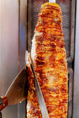 Gyros or doner, Middle East traditional food. Man's hands holding a knife, cutting slices from a vertical skewer