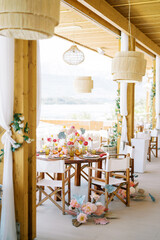 Colorful bouquets of flowers stand near the chairs at the laid festive table on the hotel terrace
