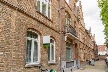 Row of renovated old brick residential buildings along a stone pavement in a historic city centre in Belgium on a cloudy summer day. A real estate sign is in foreground.