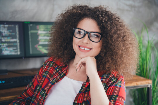 Young female programmer with curly hair working on computer in a casual checkered shirt, enjoying her workspace