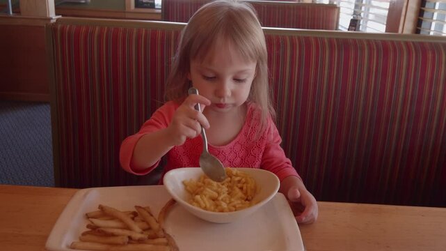 Cute Little Girl Eating Mac and Cheese in a Restaurant