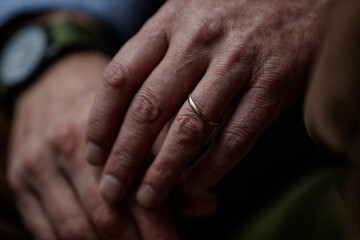 Fototapeta premium Close-up of elderly hands with wedding ring emphasizing warmth and connection. Picture captures fine details of aging hands showing wrinkles and veins