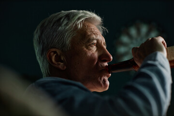 Senior man sipping from beverage bottle, reflecting in moment of enjoyment, with gray hair under...