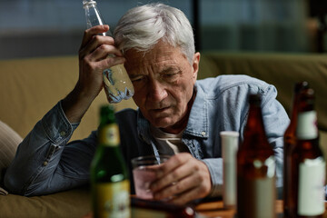 An elderly man with grey hair holding an empty bottle and looking troubled. Surrounded by various...