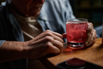 Senior person savoring a pink beverage in a dimly lit setting, captured holding drink with both hands, creating a warm and inviting atmosphere
