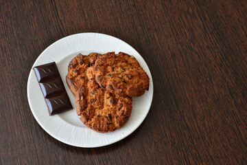 Cookies and chocolate on a white plate on wooden surface