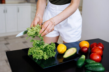 female hands tearing lettuce leaves for salad on the background of a tray with vegetables