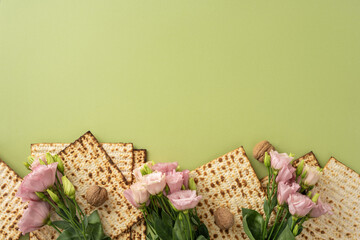 Decorative arrangement of Passover matzah flatbreads and pink flowers placed on a green background,...