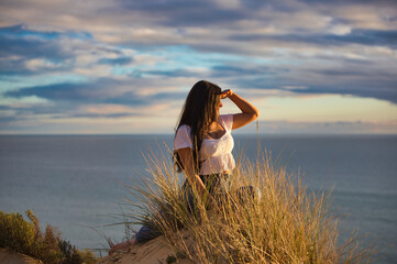 Young and beautiful Latin woman, brunette, sitting on a fine white sand dune among the reeds. The...