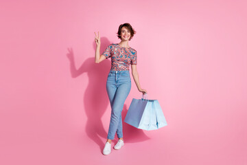 Photo of lovely cute girl wear stylish print clothes hold bags v-sign isolated on pink color...