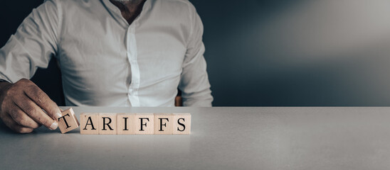 hand posing wooden blocks with the word Tariffs ,concept of trade tariffs ,economy , politics and government on a grey background