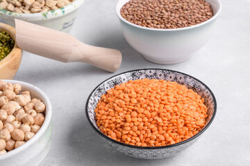 Raw red lentils in ceramic bowl on a light gray table and mixed pulses for healthy and balanced diet, plant-based protein sources, close up