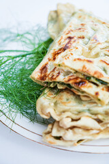 Golden-brown flatbreads with green fillings sit on a plate, topped with fresh herbs