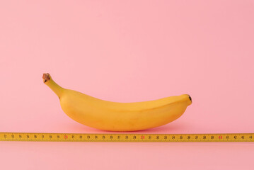Banana size is being measured with a yellow measuring tape on pink background