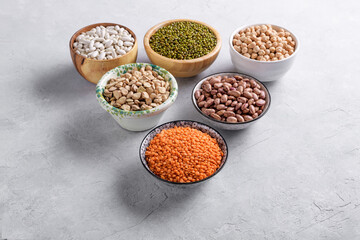 Mixed legumes for vegetarian and vegan cooking on gray table. Red lentins, White beans, green mung beans, cranberry beans in the bowls, pulses for healthy balanced diet, plant-based protein source