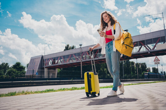 Full body photo of adorable girl device taxi app suitcase railway station wear white shirt enjoying free time sunny weather outdoors city