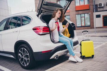 Full body photo of cute adorable girl sit car trunk drink coffee device wear white shirt enjoy free...