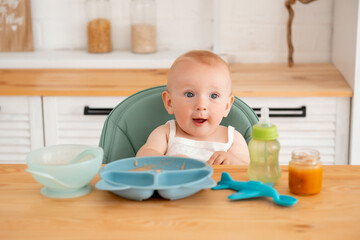 a baby boy eats baby puree in a high chair, a small child eats on his own with a spoon, baby food