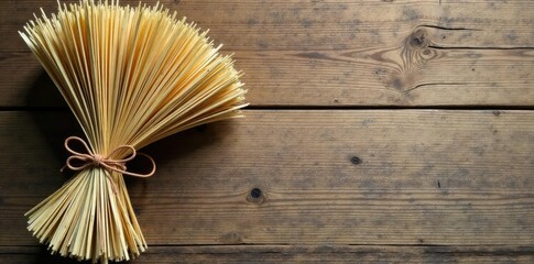 Twisted natural straw sheaf decorative bow tied with a thin leather thong on a rustic wooden background, twine, country decor