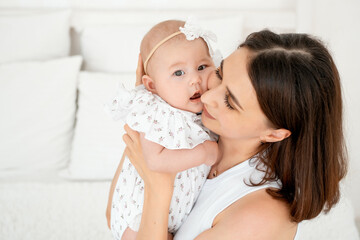 mom with a baby, an international family, a Caucasian mom with an Asian baby in her arms in the bedroom gently hugs him holding him in her arms, a place for text