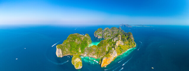 Aerial panoramic beautiful view from afar of Phi phi island ring of steep limestone cliff hills surrounding Maya Bay white beaches and coral reefs around, boats floating nearby.