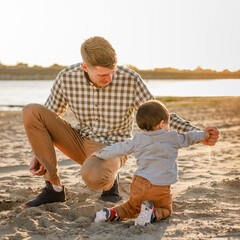 Young father playing in the sand with his little son at the riverbank on a warm day