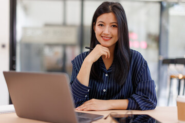  Asian businesswoman sits at desk with laptop online using internet and notepad happily recording receipt contact information online delivery.
