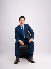 Full body image of Asian male businessman wearing a suit sitting on a chair and posing on a white...