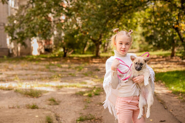 Obraz premium Blonde girl in a white poncho holding a small dog in a warm, sunny, old park