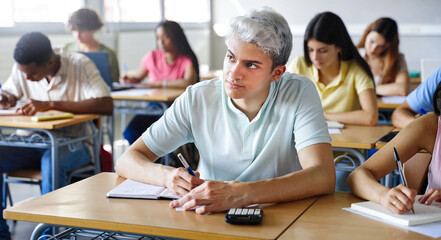 Young hispanic student taking notes during High School lesson in classroom with classmates