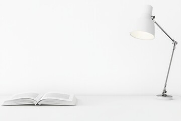 single open textbook lies on stark white desk surrounded by minimal clutter with sleek modern lamp casting gentle light