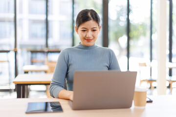 Fototapeta premium A smiling woman working on a laptop while sitting on a couch with a coffee cup, using the internet in a casual business environment