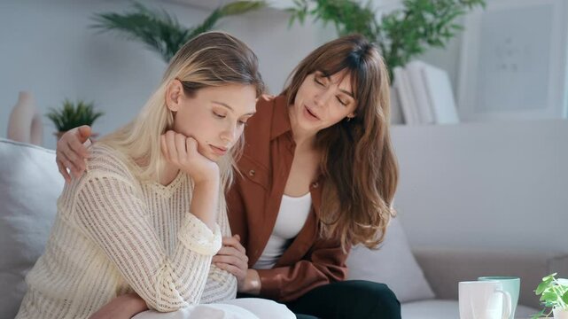 Video of pretty young woman supporting and comforting her sad friend while sitting on the sofa at home.