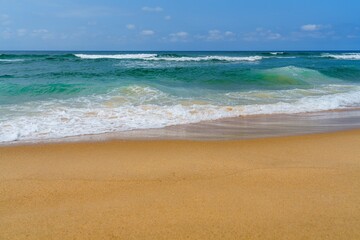 This photo features a stunning sandy beach with golden sand, clear turquoise water, and swaying palm trees under a bright blue sky, making it an ideal tropical paradise for relaxation.