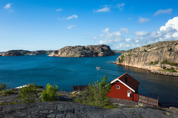 Scenic view of Hamburgsund, Sweden, featuring a red wooden house by the rocky coast, blue sea,...