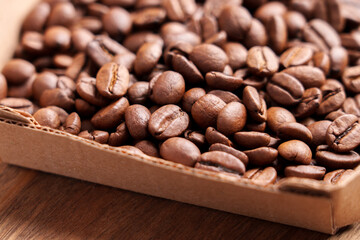 Light roast Arabica coffee beans in kraft paper box on wooden surface. Aromatic drink grains in cardboard packaging. Macro shot. 