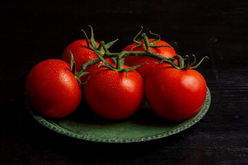 Close-up of wet tomatoes on green plate on dark table, horizontal with copy space