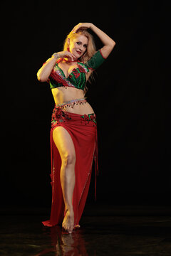 Young woman belly dancer in a red oriental costume on a black background