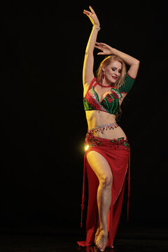 Young woman belly dancer in a red oriental costume on a black background