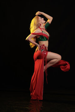 Young woman belly dancer in a red oriental costume on a black background