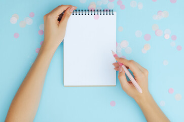 Well-groomed female hands with a pen near a notebook on a blue background. To-do list. Notes. Blank sheet for text.