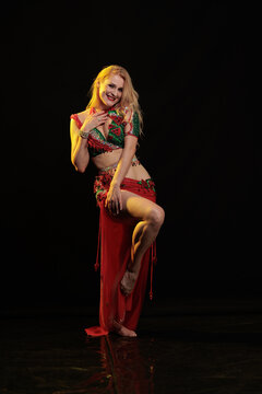 Young woman belly dancer in a red oriental costume on a black background