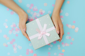 Well-groomed female hands hold a gift on a blue background. Festive background. Surprise.