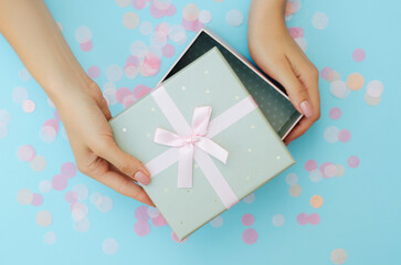 Well-groomed female hands hold a gift on a blue background. Festive background. Surprise.