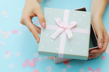 Well-groomed female hands hold a gift on a blue background. Festive background. Surprise.